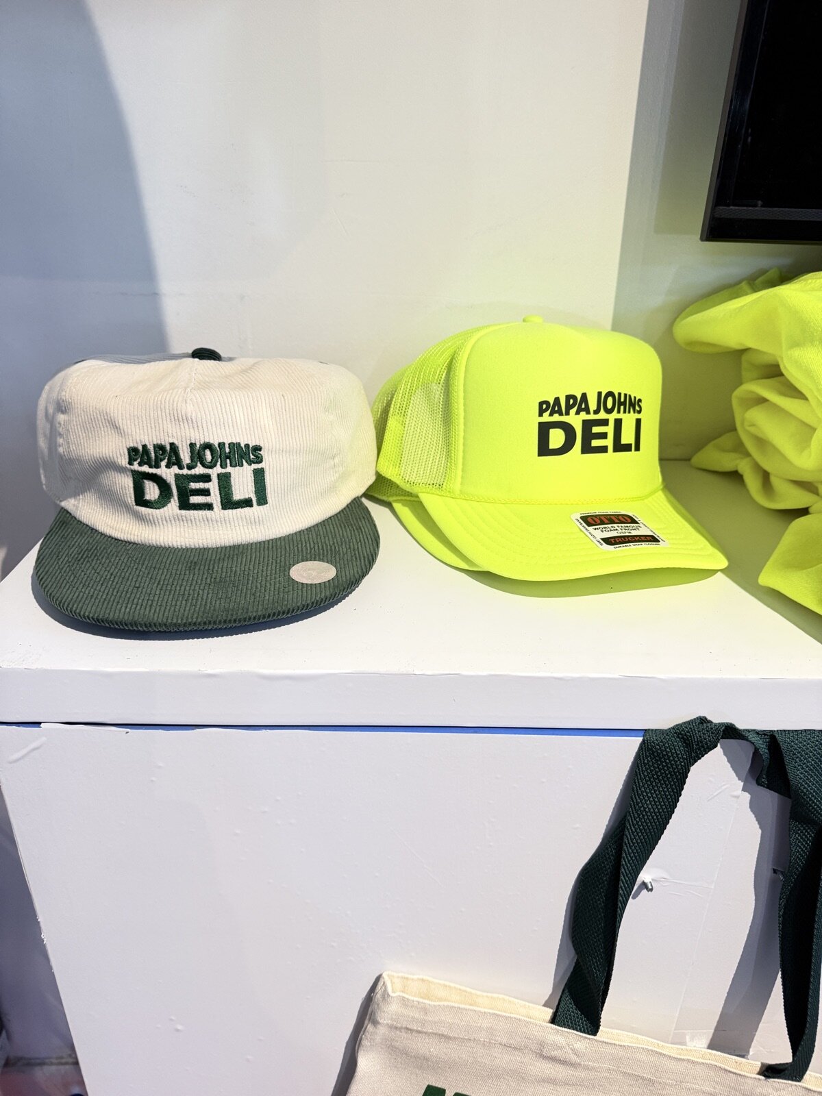 Embroidered corduroy cap and neon trucker hat displayed on a white plinth at a franchise convention