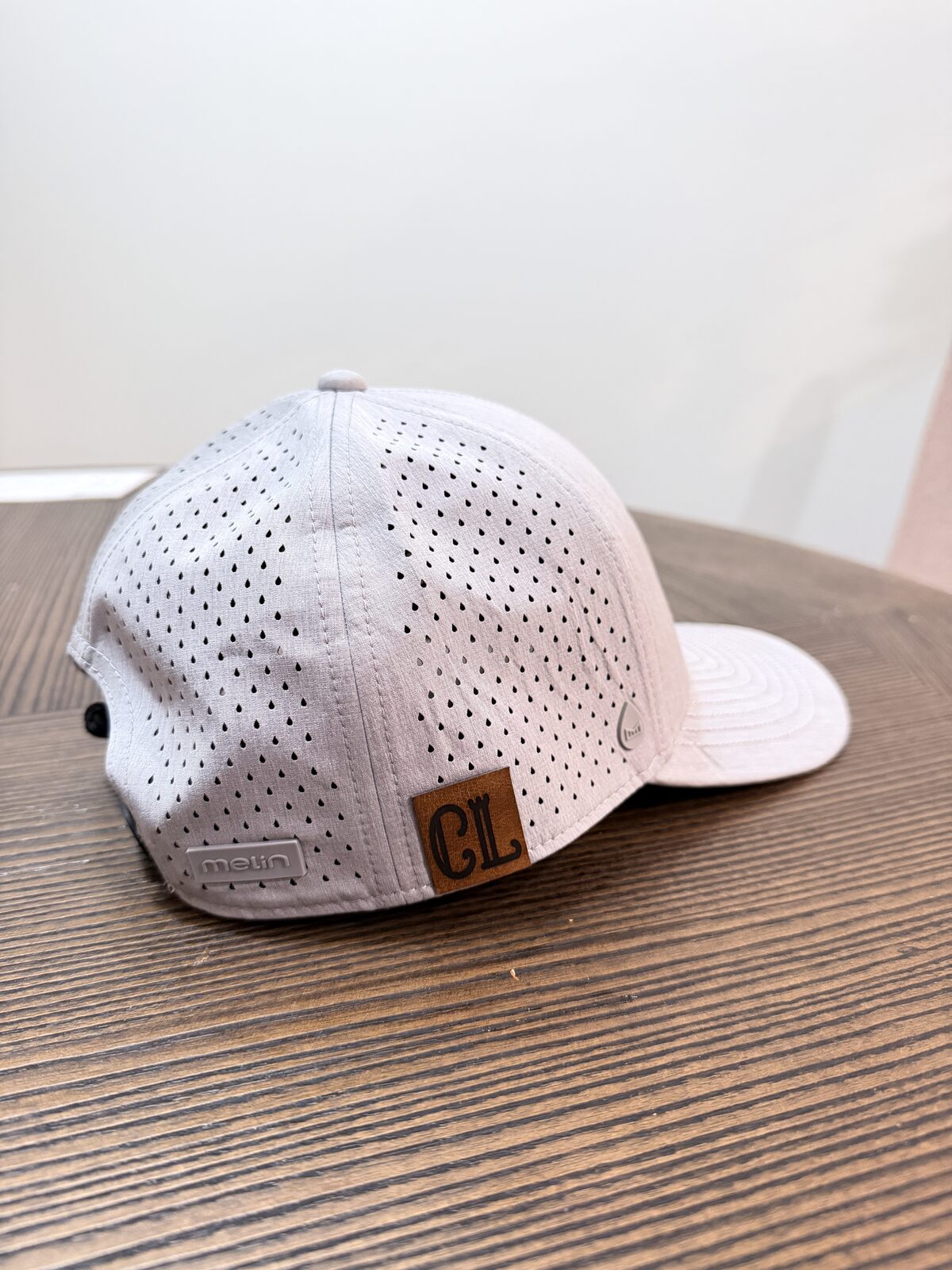 White perforated performance cap with a custom leather patch resting on a wood table