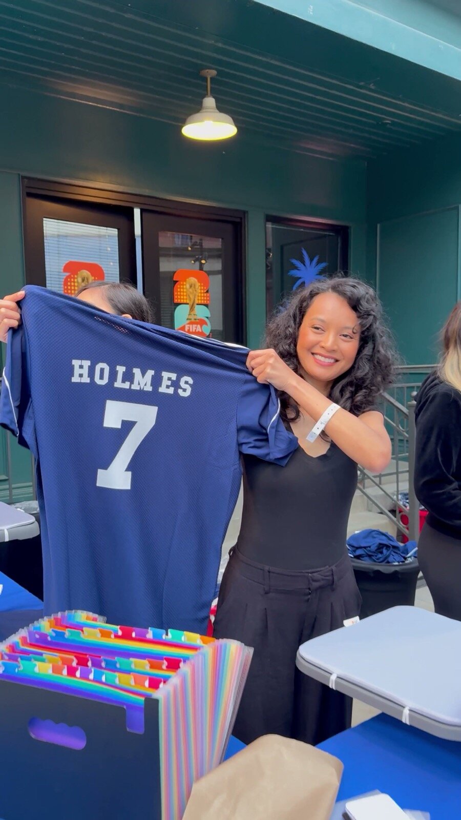 Smiling guest holding up a navy jersey personalized with her name and number at an outdoor activation