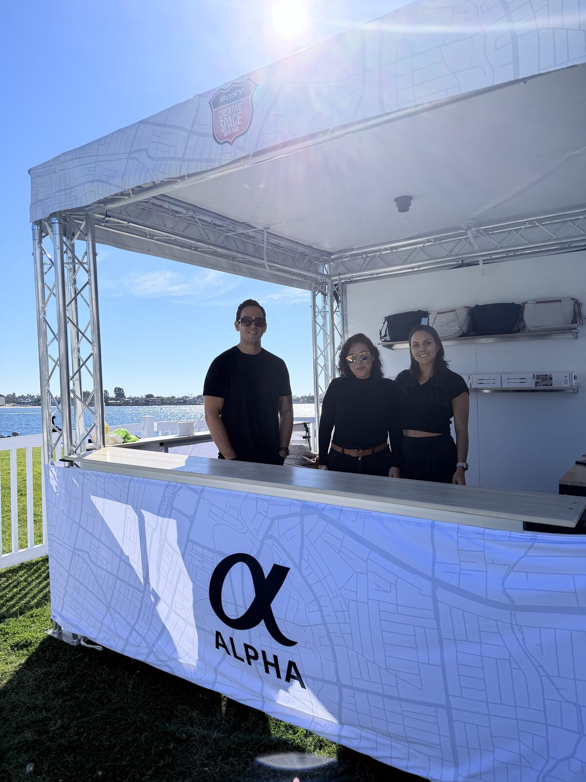 White truss brand booth with a wrapped counter and crew serving guests outdoors in full sun